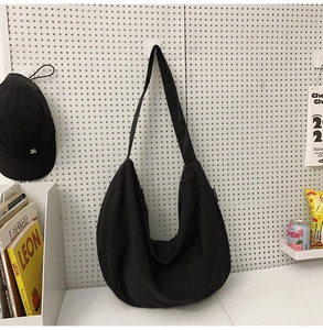 Close-up of black crescent nylon shoulder bag with wide strap on a studio pegboard