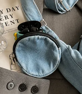 Detail of light blue denim mini pouch charm with zipper holding wireless earphones