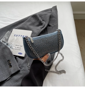 Close-up of blue denim crescent bag featuring punk-style silver rivets and metal chain strap