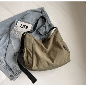 Olive green large canvas crossbody bag shown in a lifestyle scene on white sheets