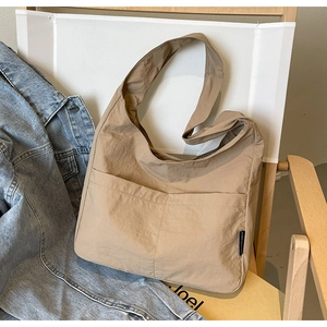 Detail of khaki nylon tote bag featuring front pockets and side brand label on denim jacket