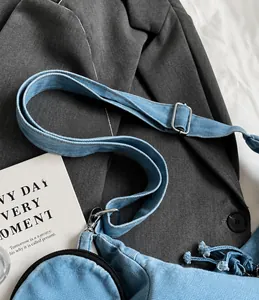 Detail of blue denim shoulder bag showing adjustable strap and silver metal buckle