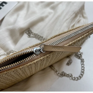 Close-up of beige straw woven clutch featuring silver zipper and fine metal chain strap