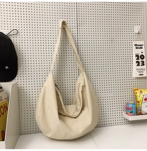 Detail of a minimalist cream-white crescent nylon shoulder bag on a pegboard background