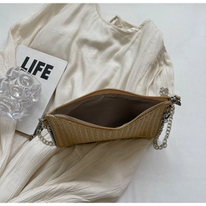 Close-up of woven straw handbag with silver metal chain and gray fabric inner lining