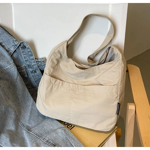 Detail of minimalist beige nylon underarm bag showing brand label and front pocket texture