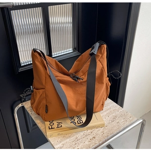 Detailed macro view of large caramel orange nylon crossbody bag with side drawstring pocket