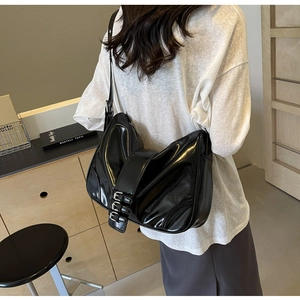 Detail of glossy black moon bag featuring silver buckles and polished leather texture
