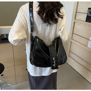 Detail of black glossy leather shoulder bag with industrial metal buckles on a model