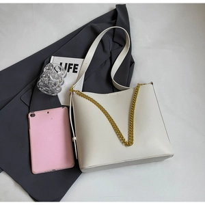Detail view of white minimalist tote bag on grey fabric with golden chain strap decoration