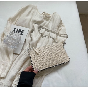 Detail of beige straw woven crossbody bag with silver bead trim and metal chain strap