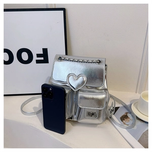 Close-up of mini silver metallic backpack with heart detail and chain handle next to phone
