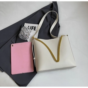 Detail view of cream tote bag with gold chain strap on grey blazer for professional style