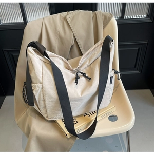 Detail view of beige canvas shoulder bag with adjustable black strap on a chair
