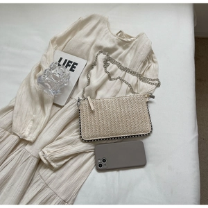 Detail of cream straw woven shoulder bag with silver beads and chain strap for summer style