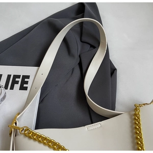 Detail of white leather tote bag featuring gold chain and adjustable shoulder strap