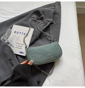 Detail of blue denim shoulder bag with thick silver chain link on grey suit background