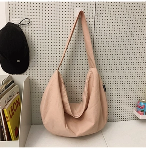 Detail of light pink nylon tote bag with crescent shape and zip closure on a wall rack