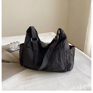 Detail view of black canvas crossbody bag showing side pockets and metal strap buckle