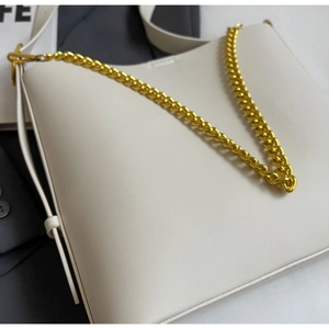 Close-up of cream shoulder bag with chunky gold chain detail and textured finish