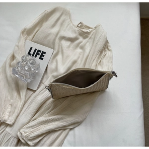 Detailed shot of cream woven straw clutch bag with silver chain trim and tan lining