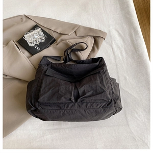 Close-up of black canvas messenger bag with large flap pockets on a beige blazer