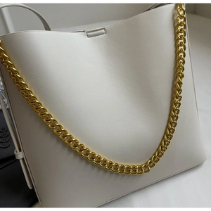 Close-up of minimalist white bucket bag featuring a thick gold metal chain detail