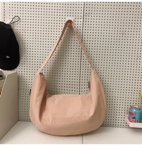 Detail of light pink crescent nylon tote bag with wide strap on a white pegboard background
