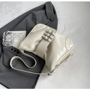 Close-up of creamy white patent leather shoulder bag with triple metal buckle straps