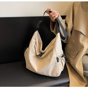 Detail of beige nylon crossbody bag featuring black webbing strap and drawstring closure