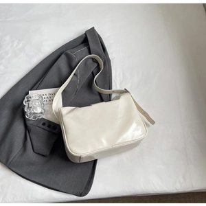 Minimalist creamy white shoulder bag in smooth leather on a bed with grey suit