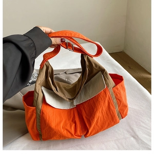 Detail view of canvas crossbody bag showing orange and brown color-blocking and front pocket