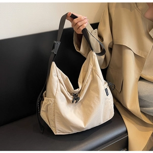 Detail of beige nylon tote bag featuring adjustable black strap and knot zipper pull
