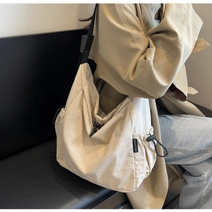 Detail of cream canvas messenger bag showing black shoulder strap and side drawstring pocket