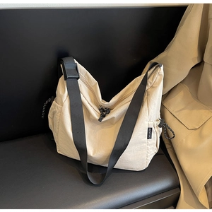 Detail of off-white nylon crossbody bag with adjustable strap on a dark leather bench
