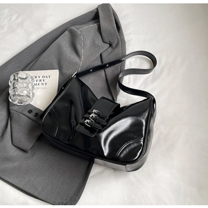 Detail shot of black patent leather hobo bag with three silver buckles on white background
