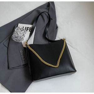 Detail of black leather tote bag with thick gold chain strap and modern minimalist design