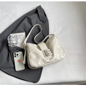 Detail of white glossy leather shoulder bag with metallic buckles on a grey blazer