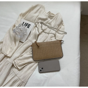 Detail of woven straw phone bag with silver bead trim and a sleek metal chain strap