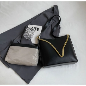 Detail of minimalist tote bag set with bold gold chain and matching pouch on fabric