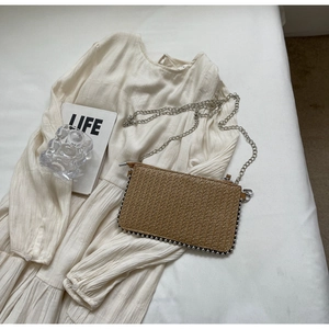 Detailed view of woven straw crossbody bag with silver rivets and metal chain strap