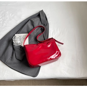 Detail of red glossy patent leather shoulder bag on grey suit and white background