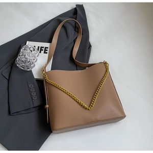 Detail of tan leather tote bag with thick gold chain strap on grey blazer background