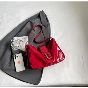 Detail of red patent leather shoulder bag with silver buckles on grey blazer background