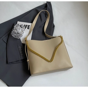 Detail view of a beige leather tote bag with gold chain strap on a grey blazer