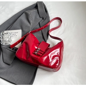 Detail of red patent leather hobo bag with triple buckle straps on grey background