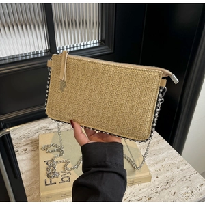 Detail of straw woven clutch bag featuring silver bead trim and a sleek chain strap