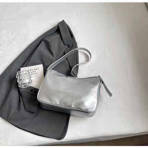 Flat lay of a metallic silver shoulder bag with mirror finish on white fabric