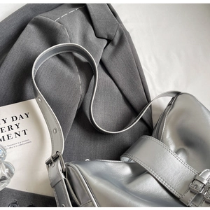 Detail of silver metallic shoulder bag featuring buckle strap on grey blazer background