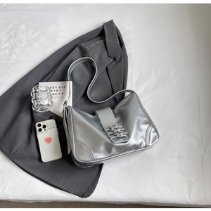 Detailed view of silver metallic shoulder bag with wide strap on a textured background